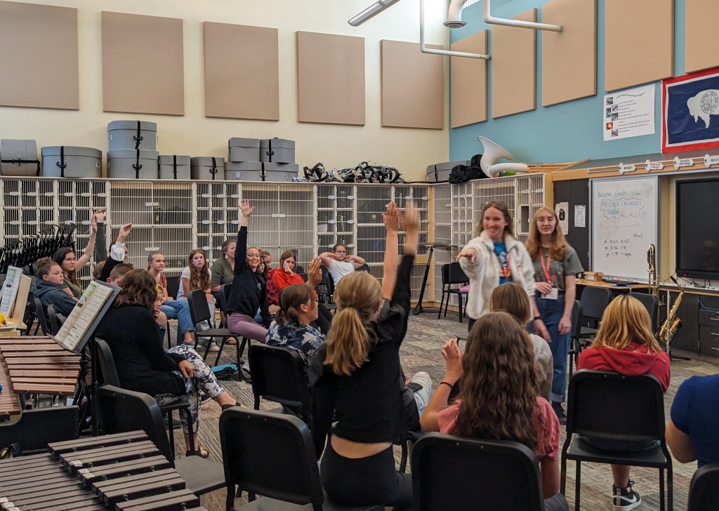 A class of children in a music classroom raises their hands to answer a question