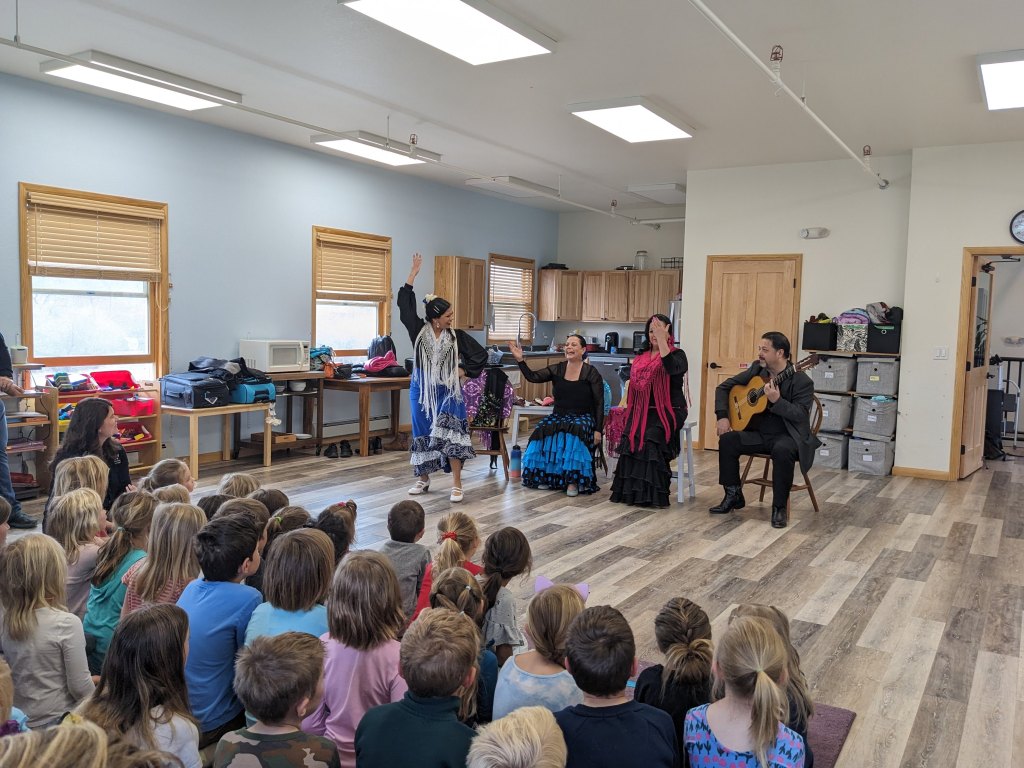 A class of children watch a group 4 women in a musical performance